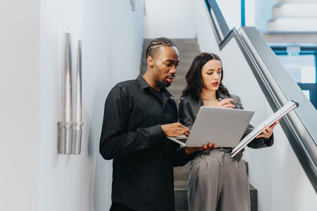 Two people discussing work with a laptop and document in a modern business setting