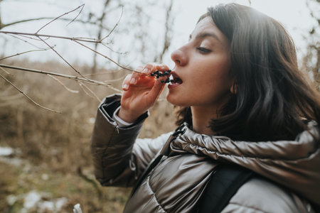 Young woman tasting berries in the wild forest during a cool autumn day