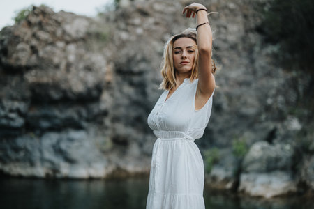 Elegant woman in white dress posing gracefully against rocky natural backgroundの写真素材