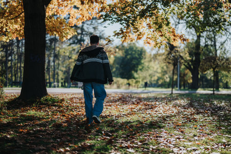 Person strolling through a sunlit autumn park with fallen leavesの写真素材