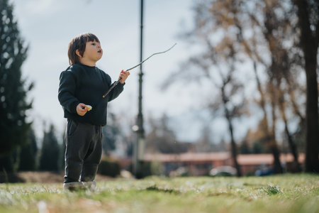 Young child playing with a stick outdoors in a sunny park setting