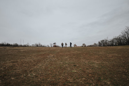 Three people walking on a wide open field under an overcast skyの写真素材