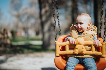 Young child joyfully swinging outdoors in a park during a sunny dayの写真素材