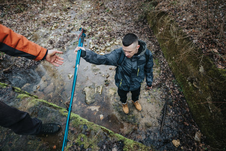 A hiker receiving a helping hand while crossing a rocky and mossy stream during an outdoor adventureの写真素材