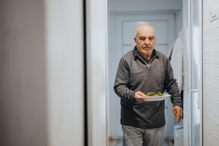 Elderly Man Carrying a Plate of Food in a Bright and Clean Home Interior Settingの写真素材