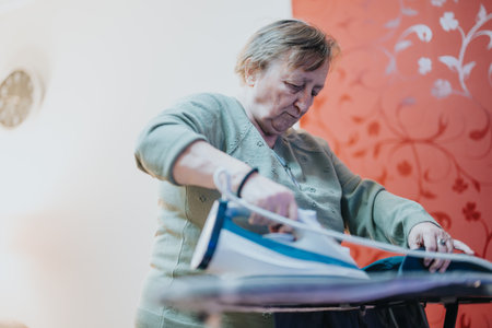 Elderly woman carefully ironing clothes at home in a cozy settingの写真素材