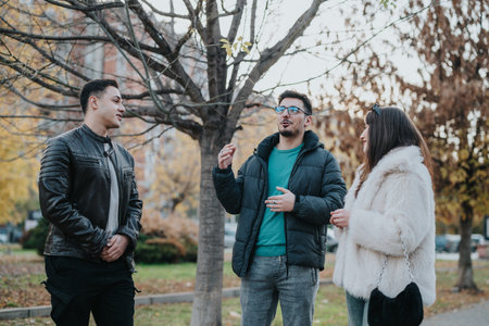 Three friends smiling and talking outdoors in a park in autumnの写真素材