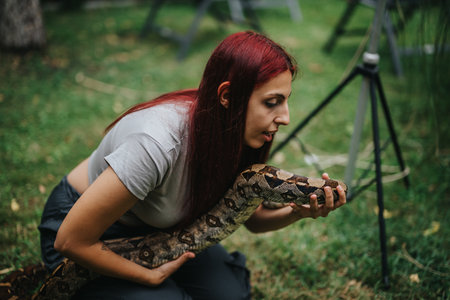 Girl gently holding a boa constrictor in a grassy areaの写真素材