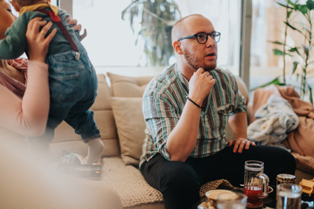 Casual moment of a man sitting indoors attentively while a baby is held nearby, creating a cozy and familial scene with warm tones and natural decor.の写真素材
