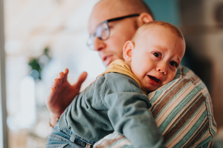 Father comforting upset baby at home, highlighting a loving parent-child bondの写真素材