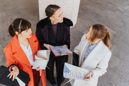Three businesswomen discussing charts and ideas outdoors in a collaborative meetingの写真素材