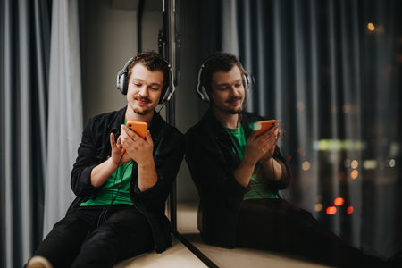 Young man enjoying music on headphones indoors while using a smart phoneの写真素材
