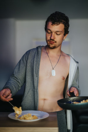 Young man in casual home attire preparing a meal in a relaxed setting.の写真素材