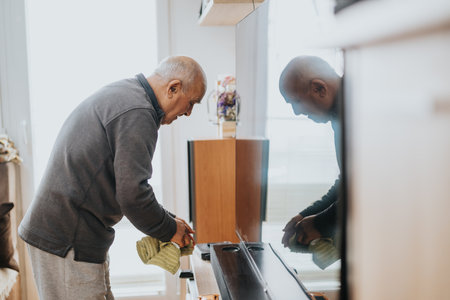 Elderly Man Polishing a Wooden Surface at Home in a Bright Room, Reflecting His silhouetteの写真素材