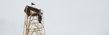 Person climbing a lookout tower in a peaceful outdoor setting under a cloudy skyの写真素材