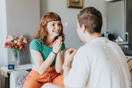 Young woman in a green shirt joyfully interacting with a seated friend in a bright home.の写真素材