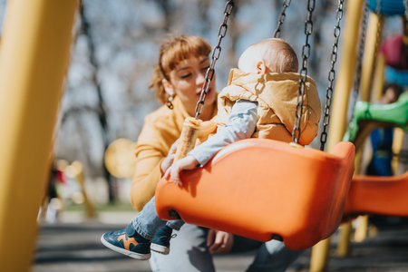 Mother and young child enjoying time on a swing at a parkの写真素材