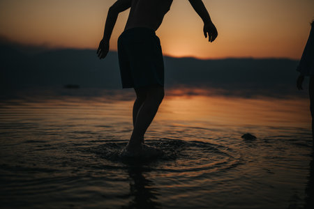 Silhouette of a person at sunset splashing water in a serene lakeの写真素材