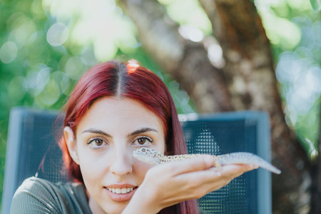 Young girl with red hair gently holding a lizard outdoors, enjoying a playful interaction under natural sunlightの写真素材