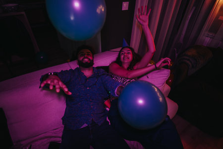 Friends enjoying a lively birthday party at home with balloons and laughterの写真素材
