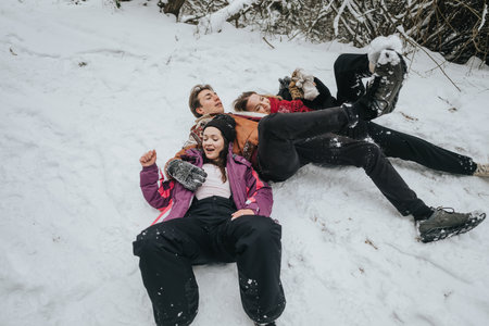 Three friends enjoy a playful moment together lying in the snow during a winter outingの写真素材