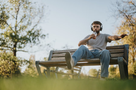 Man relaxing on park bench listening to music and sipping a drinkの写真素材