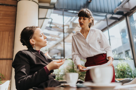 Two businesswomen engaged in a professional conversation during a meeting at a cafe.の写真素材