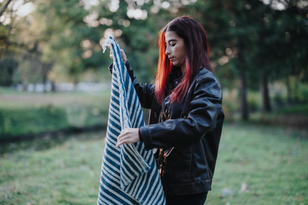Young woman folding a blue and white blanket outdoors in a parkの写真素材