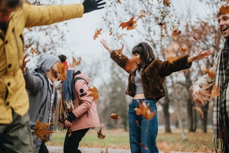 Friends enjoying an autumn day in the park playing with falling leavesの写真素材