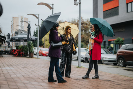 Group of women with umbrellas chatting on a rainy city dayの写真素材