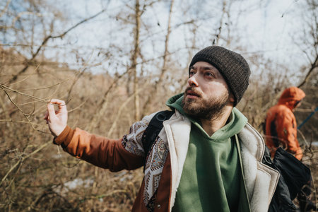 Man exploring a natural outdoor setting, wearing warm clothing and observing surroundings in a wooded area with bare treesの写真素材