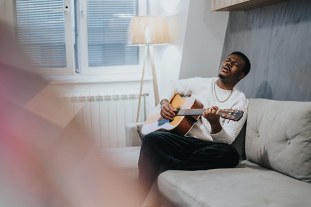 Man playing acoustic guitar with passion while sitting on a cozy sofa at home