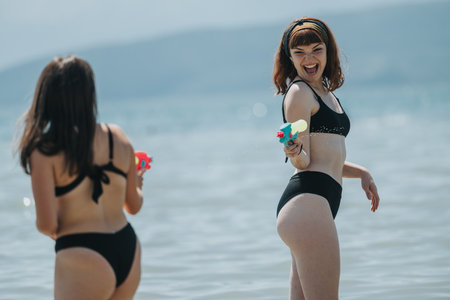 Two friends playing with water guns in the summer at the beachの写真素材