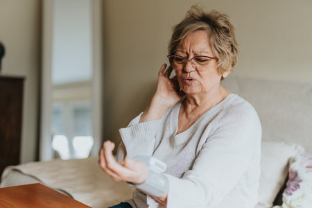 Senior Woman Using a Blood Pressure Monitor While Sitting on Her Bed at Homeの写真素材
