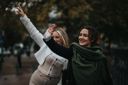 Two women happily waving on a street in an outdoor autumn setting