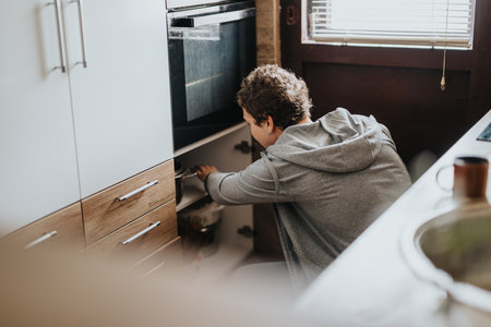 Young man organizing kitchen cabinets in a modern and warm home environment