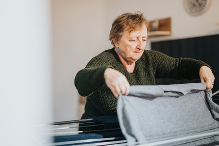 Elderly woman hanging clothes indoors showcasing everyday tasksの写真素材