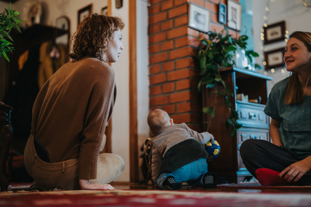 Two women sitting indoors with a baby holding a ball, creating a cozy and joyful family atmosphere.の写真素材