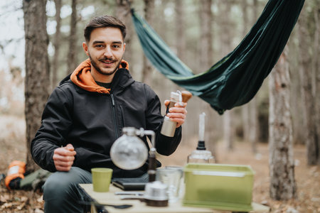 Man Camping in Forest Setting Preparing Coffee With Hammock and Equipmentの写真素材