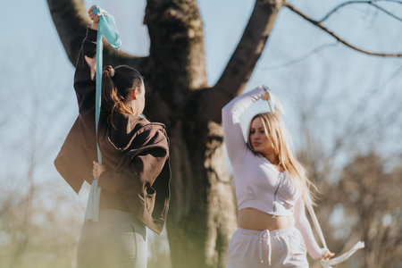 Two individuals exercising outdoors in a park using resistance bands