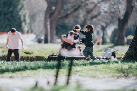 Child playing outdoors in a sunny park setting with family members nearbyの写真素材