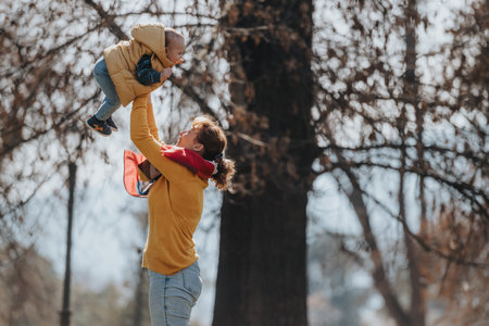 Mother lifting child in autumn park, enjoying joyful bonding momentの写真素材