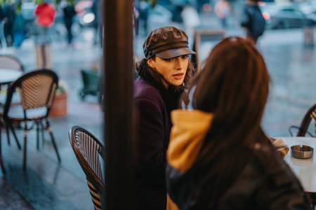 Two individuals conversing outdoors at a cafe on a rainy day in the cityの写真素材