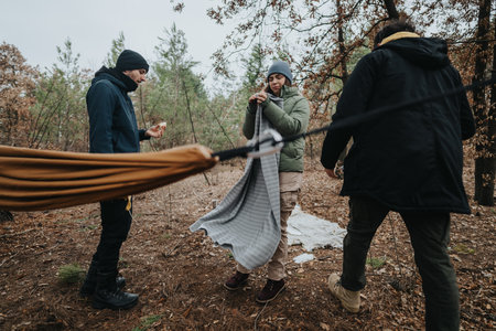 Young friends setting up camp in forest clearing during a chilly dayの写真素材