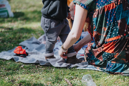 Parent assisting a toddler with shoes during outdoor picnic on a sunny dayの写真素材