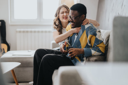 A joyful couple shares laughter and playful moments together, sitting comfortably on a couch in...