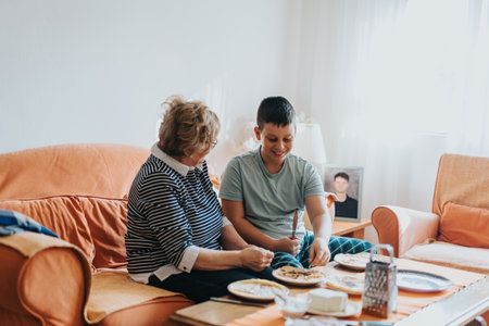 Senior woman and young boy enjoying quality time together, bonding while preparing a meal on the couch in a cozy home environment.の写真素材