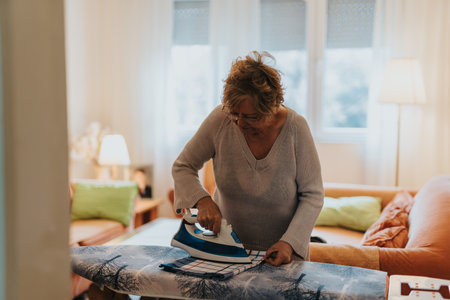 Senior woman ironing clothing in a cozy home interiorの写真素材