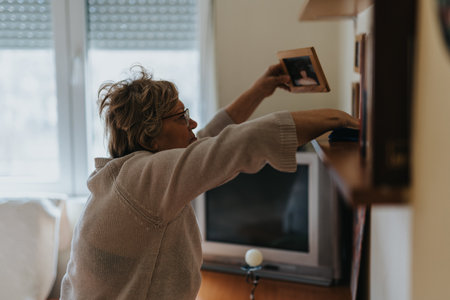 Senior woman arranging family photographs on shelves in a cozy living room