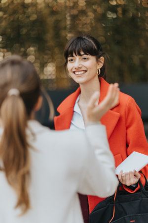 Two businesswomen interacting outdoors, having a friendly conversation